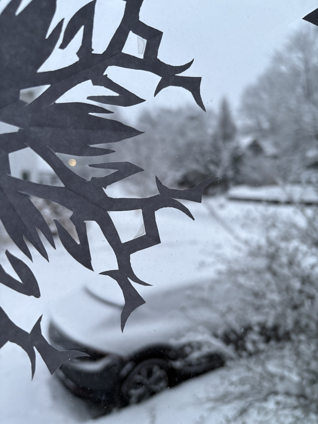 Paper snowflake on window looking out on snow-covered car and street