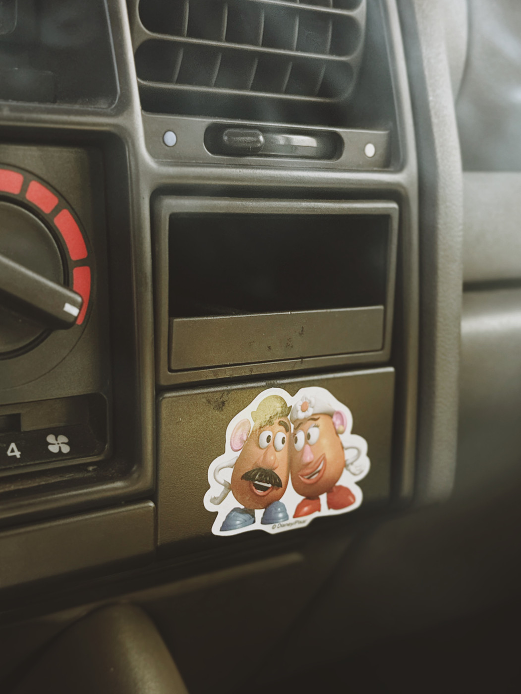 Sticker of Mr. and Mrs. Potato Head on a car dashboard near the air vent and climate control knob.