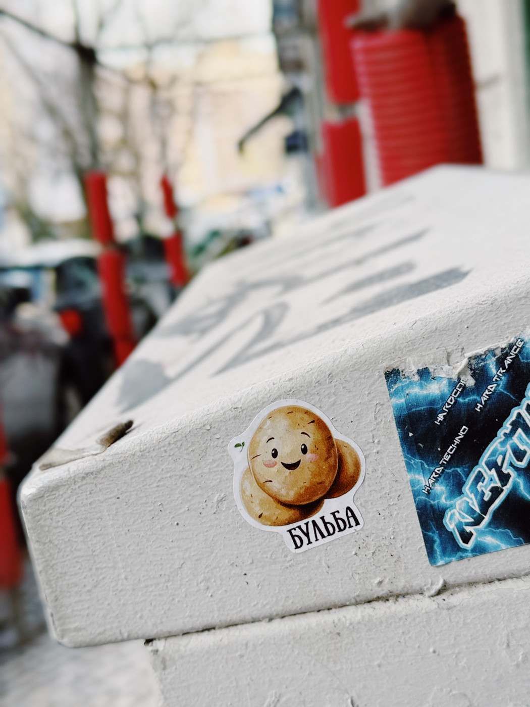 Close-up of a cute potato sticker with a smiling face and the word “Бульба” on a gray outdoor utility box.