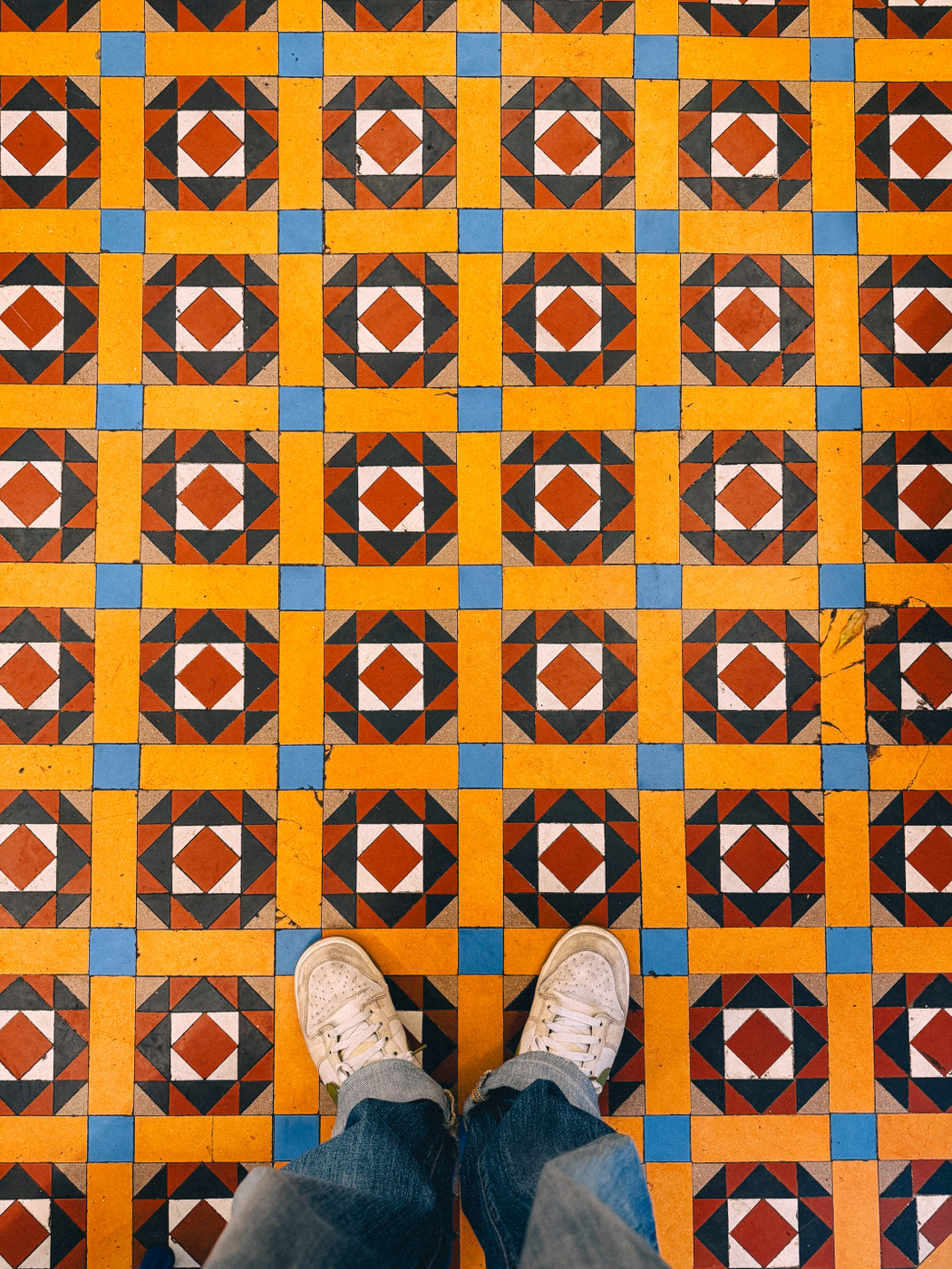 Person standing in white sneakers and jeans on a floor with colorful geometric patterns.