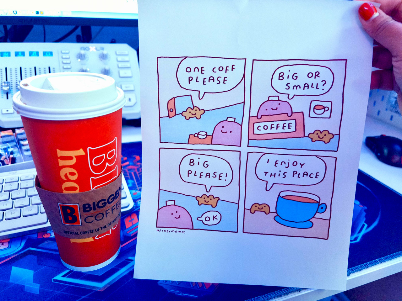 To the left is a large coffee with a red container and white top, and to the right is a comic by heyheymomo asking for a big or small “coff”, with the end comic saying “I enjoy this place.”