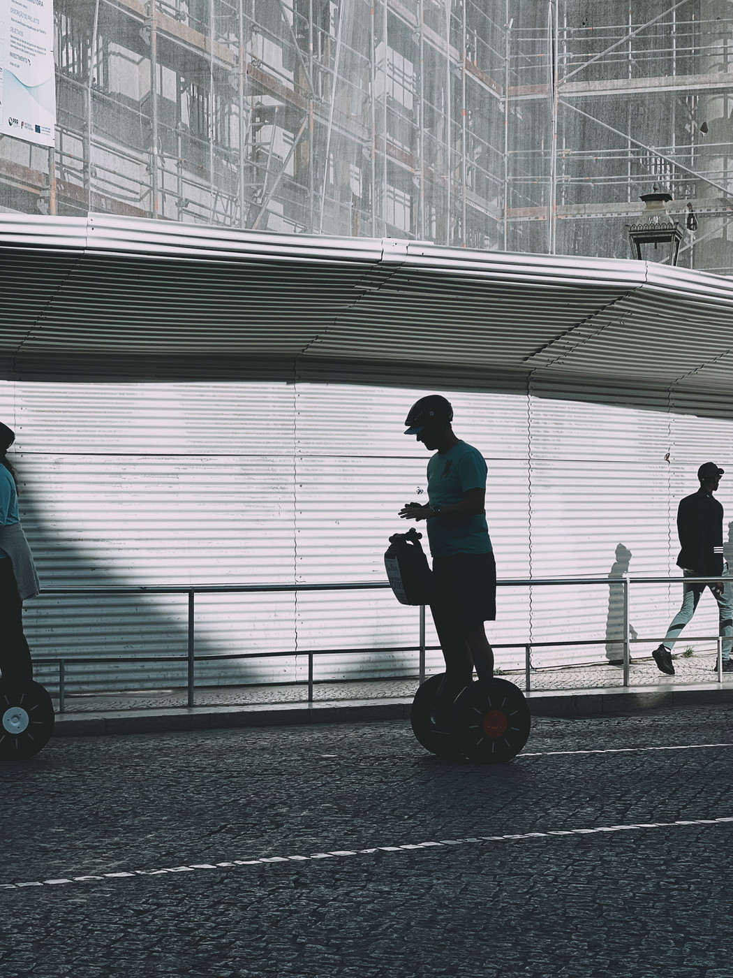 Silhouetted individuals riding Segways on a city street, with a partially constructed building and scaffolding in the background.