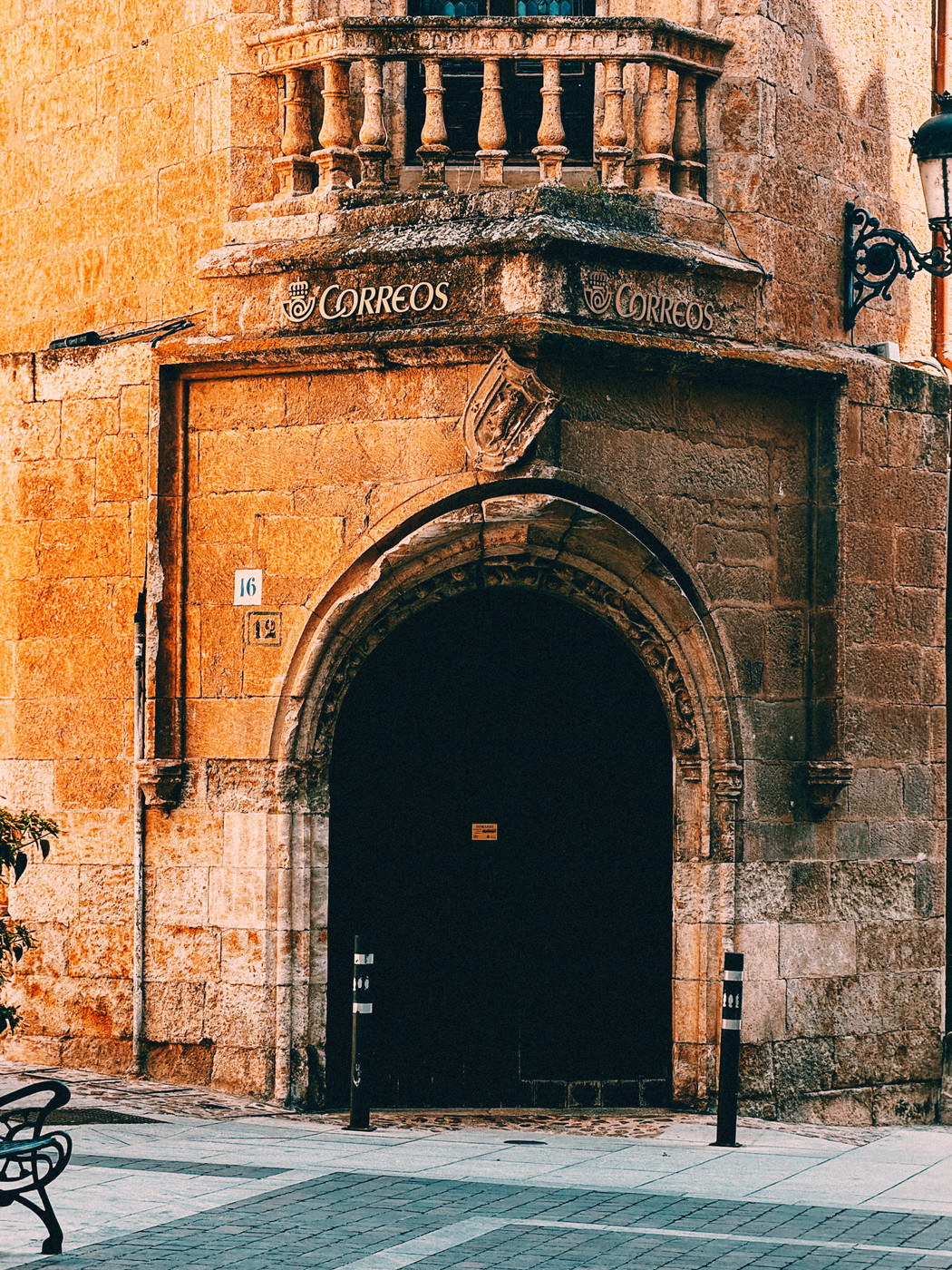 Historic stone building with an arched entrance, a small balcony with balustrades above, and the word “Correos” displayed, indicating a post office.