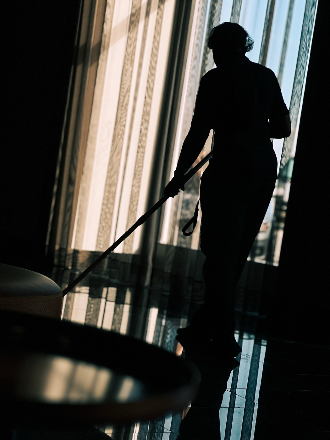Silhouette of a person cleaning a polished floor near large windows with curtains.
