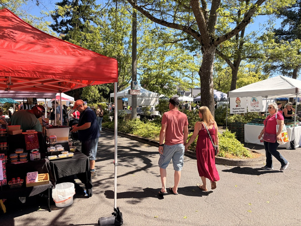 People walking in the sun, past different food booths. The one on the left has a red top and is inhabited by a guy who sold delicious-smelling cornbread that I couldn’t eat (gluten).