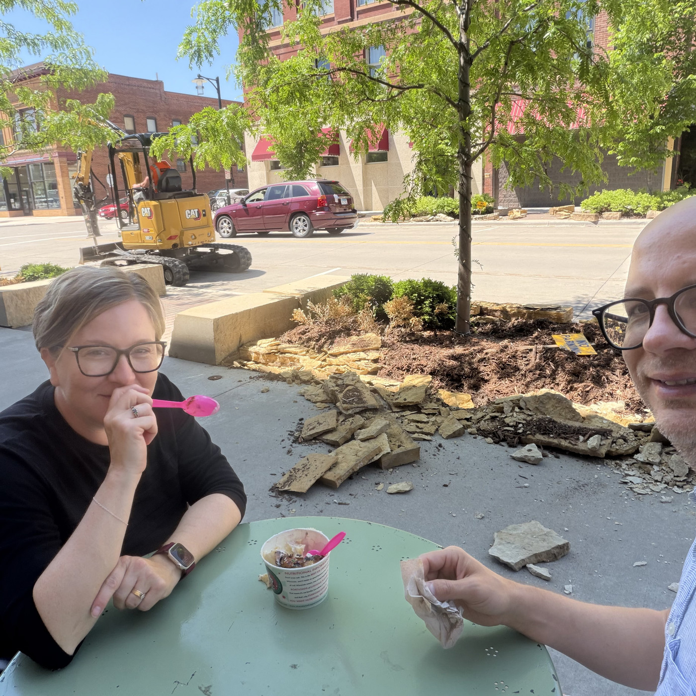 Jesse and I eating at a sidewalk table, with a mobile jackhammer and broken up rock strewn across the sidewalk.