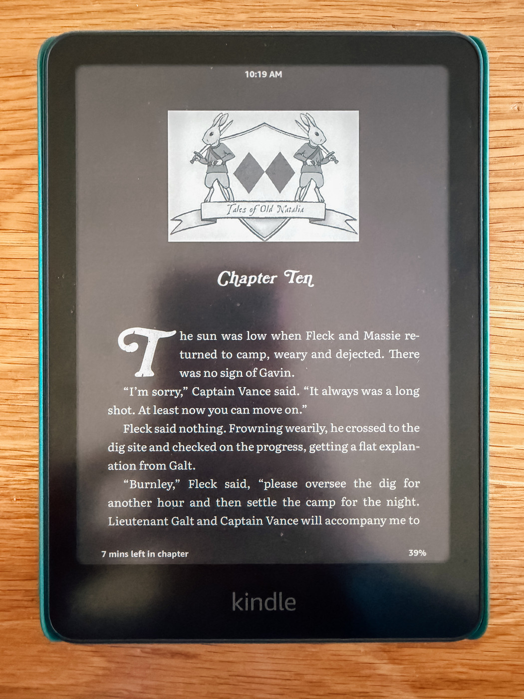 Auto-generated description: A Kindle displays a page from a book, showing Chapter Ten with the title Isle of Old Kaltak and an illustration of two rabbits holding spears above diamond shapes.