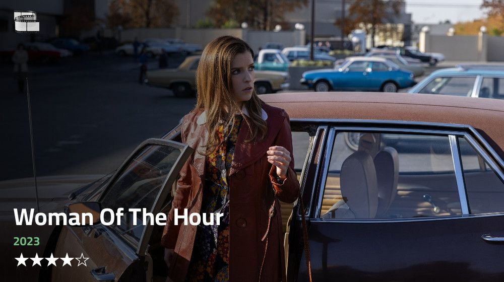 A woman stands beside the driver's side of a vintage car with the door open, holding the door handle. She wears a maroon coat over a patterned dress with a brown leather jacket. The background shows a parking lot with several parked cars, including a blue car and a beige car, along with urban buildings and trees. The text on the image reads "Woman Of The Hour" in large white letters, "2023" below it in green, and a 4-star rating symbol. There's also a small movie logo in the top left corner.