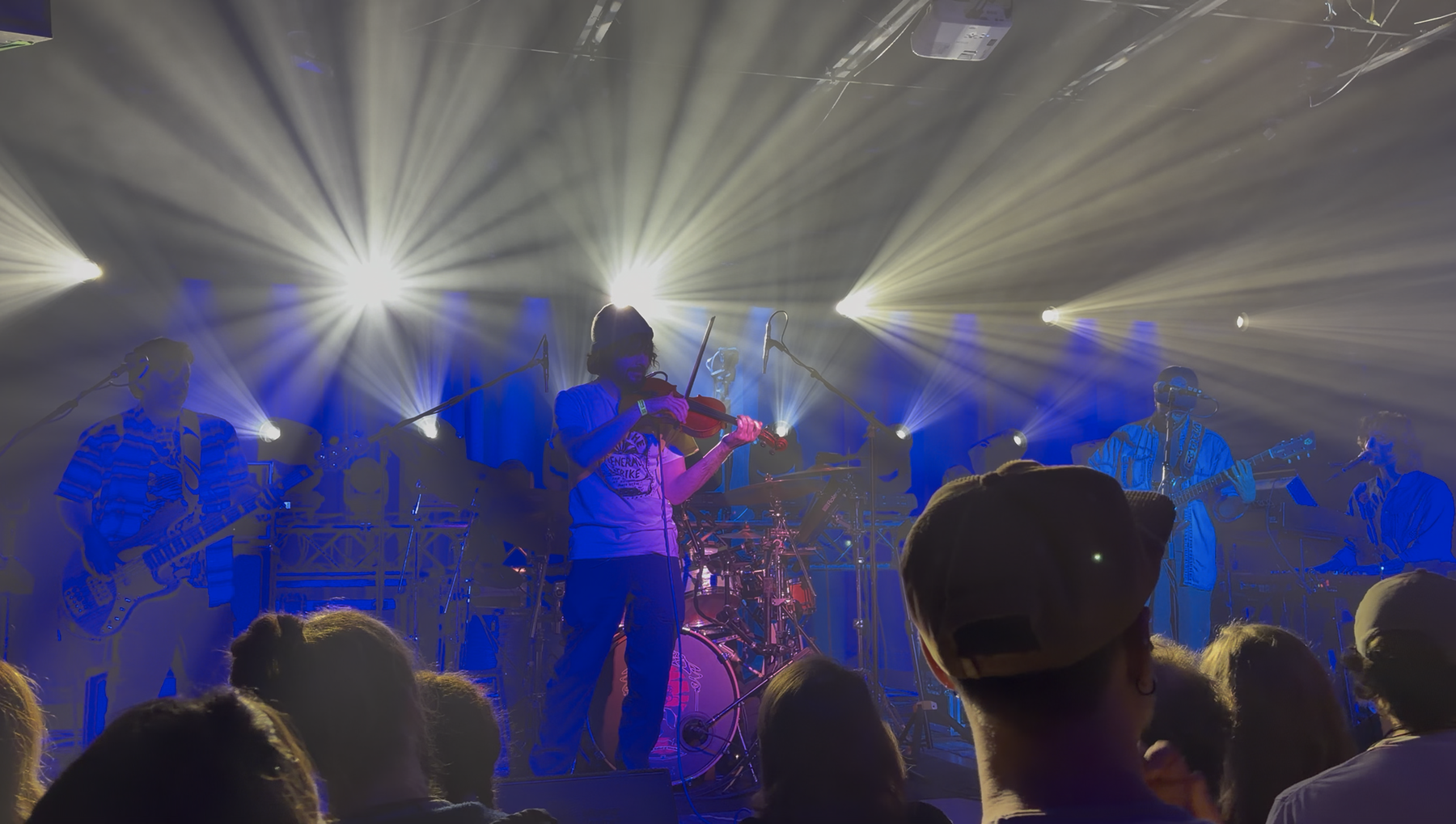 A musician playing a violin on stage with bright lights and a crowd watching.