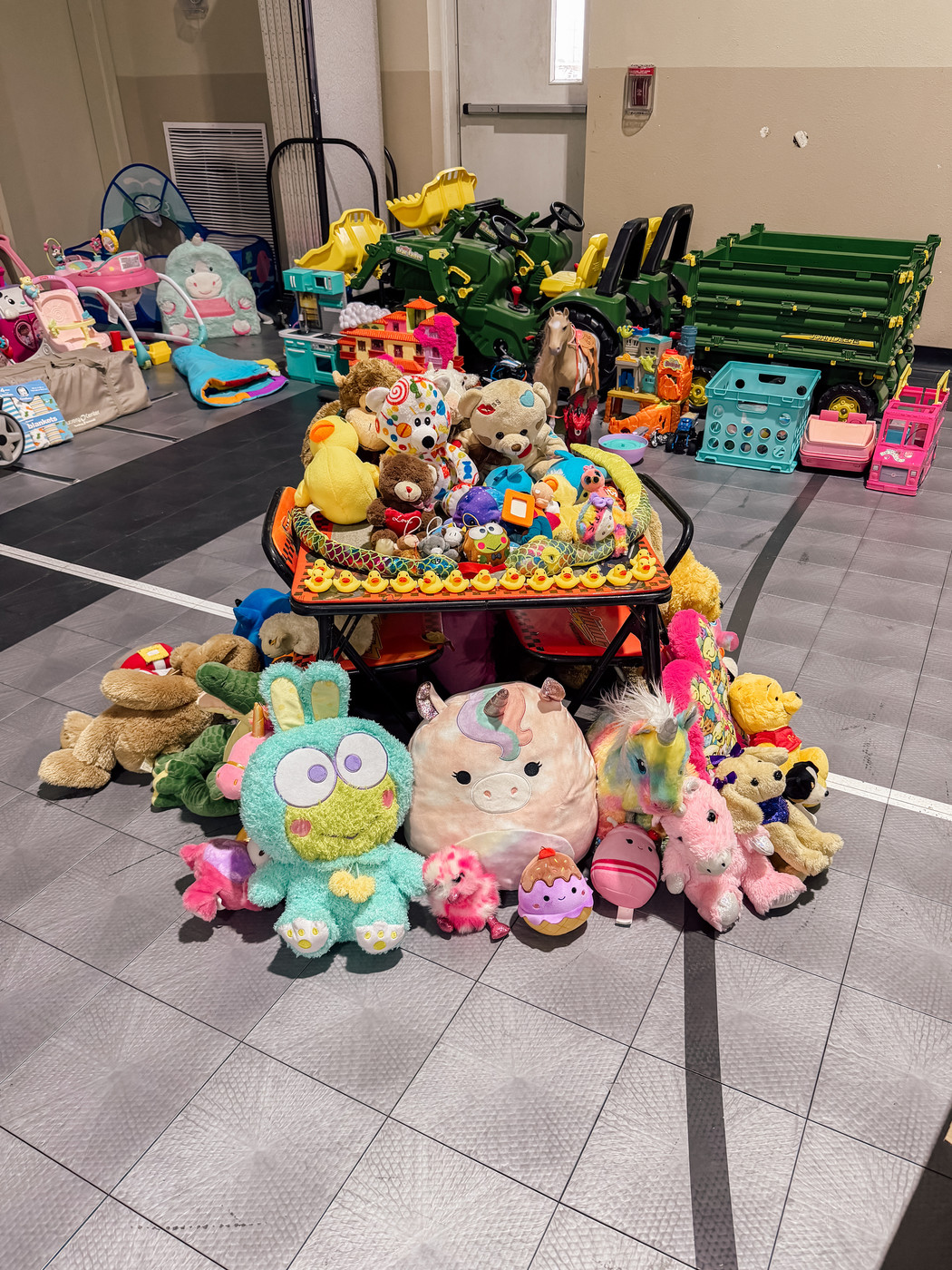 A collection of colorful stuffed animals and toys is displayed on a gym floor.