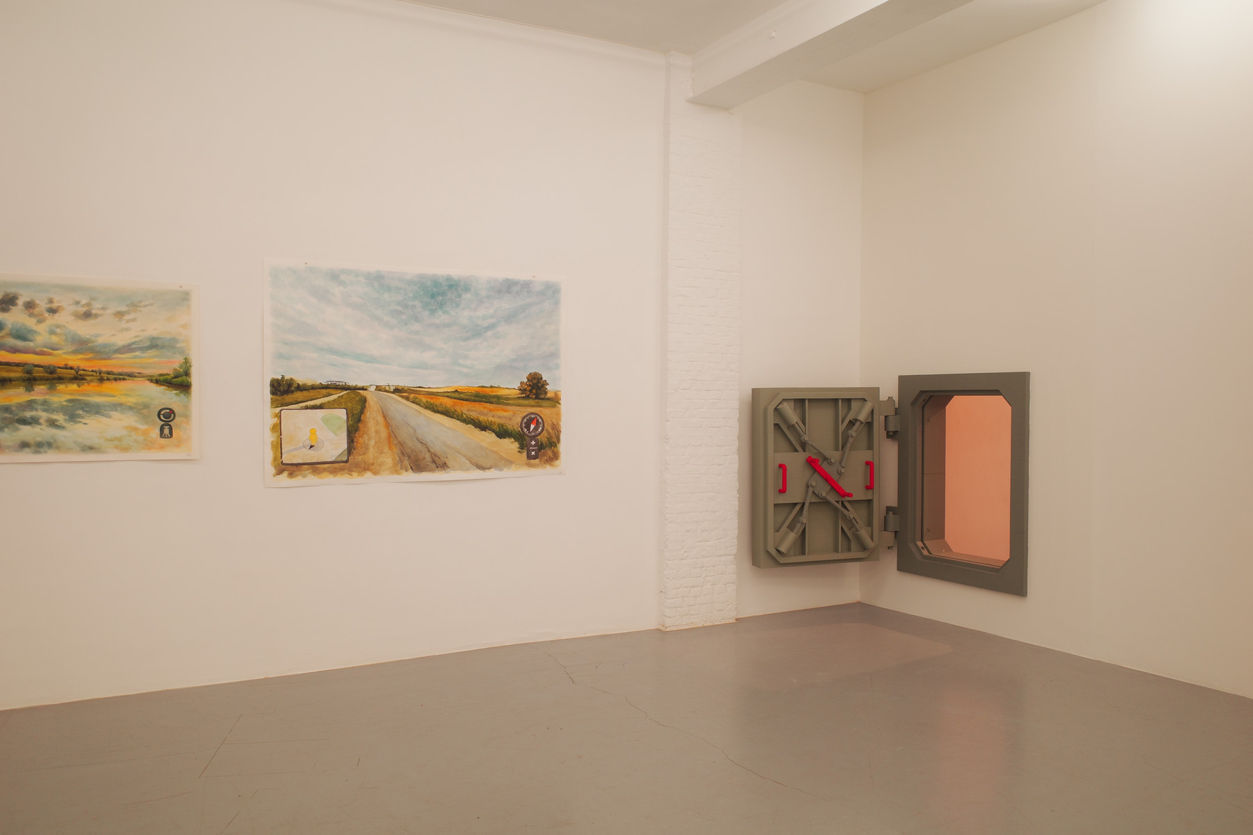 Interior of an art gallery with pale walls and a gray floor. On the left wall are two landscape paintings: the left depicts a sunset over a lake, the right shows a rural road scene. A white brick column stands between the paintings. On the right wall is a large gray metal wall sculpture with red latches and a pink rectangular opening.