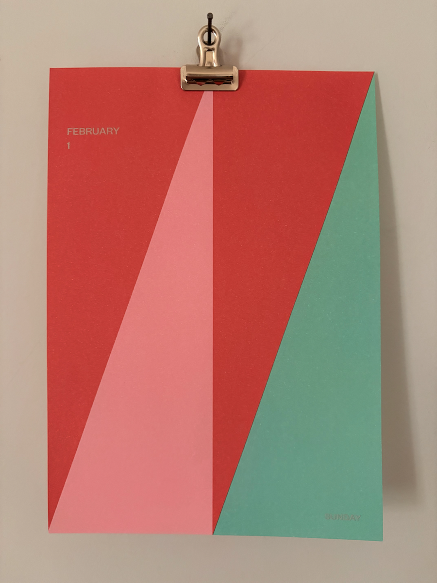 A minimalist wall calendar page clipped at the top, showing February 1 on a red background with bold geometric shapes in red, pink and teal, and the word Sunday in the bottom right corner.