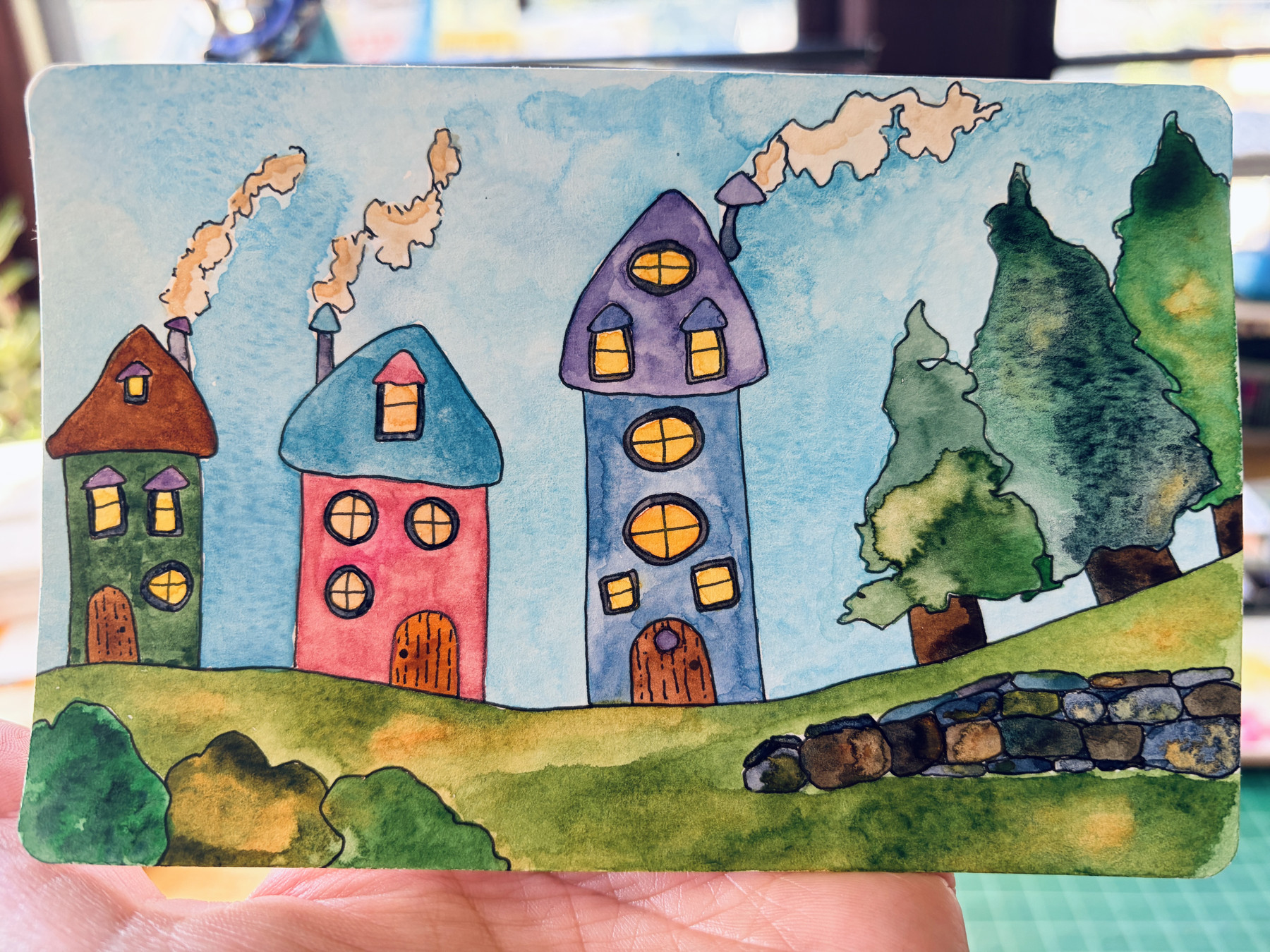 Watercolor, three little fantasy houses sitting on a horizon, three trees and a little stone wall on the right.