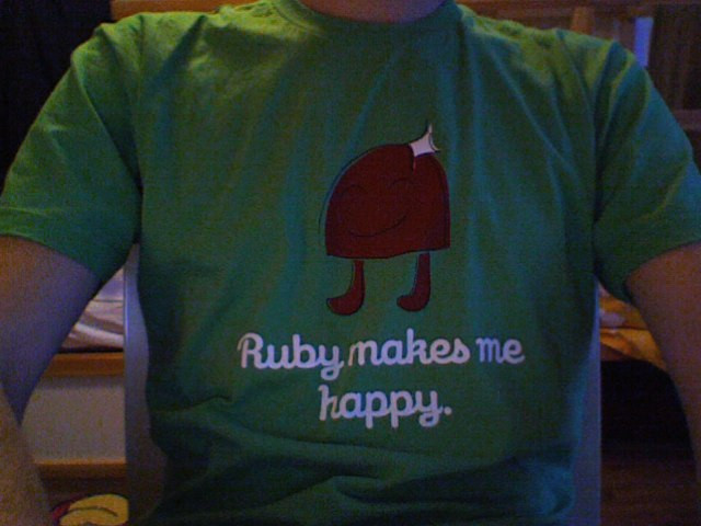 Close-up of a person wearing a green T-shirt with a red cartoon figure and the words “Ruby makes me happy” in white lettering. The photo is indoors and cropped at the shoulders.