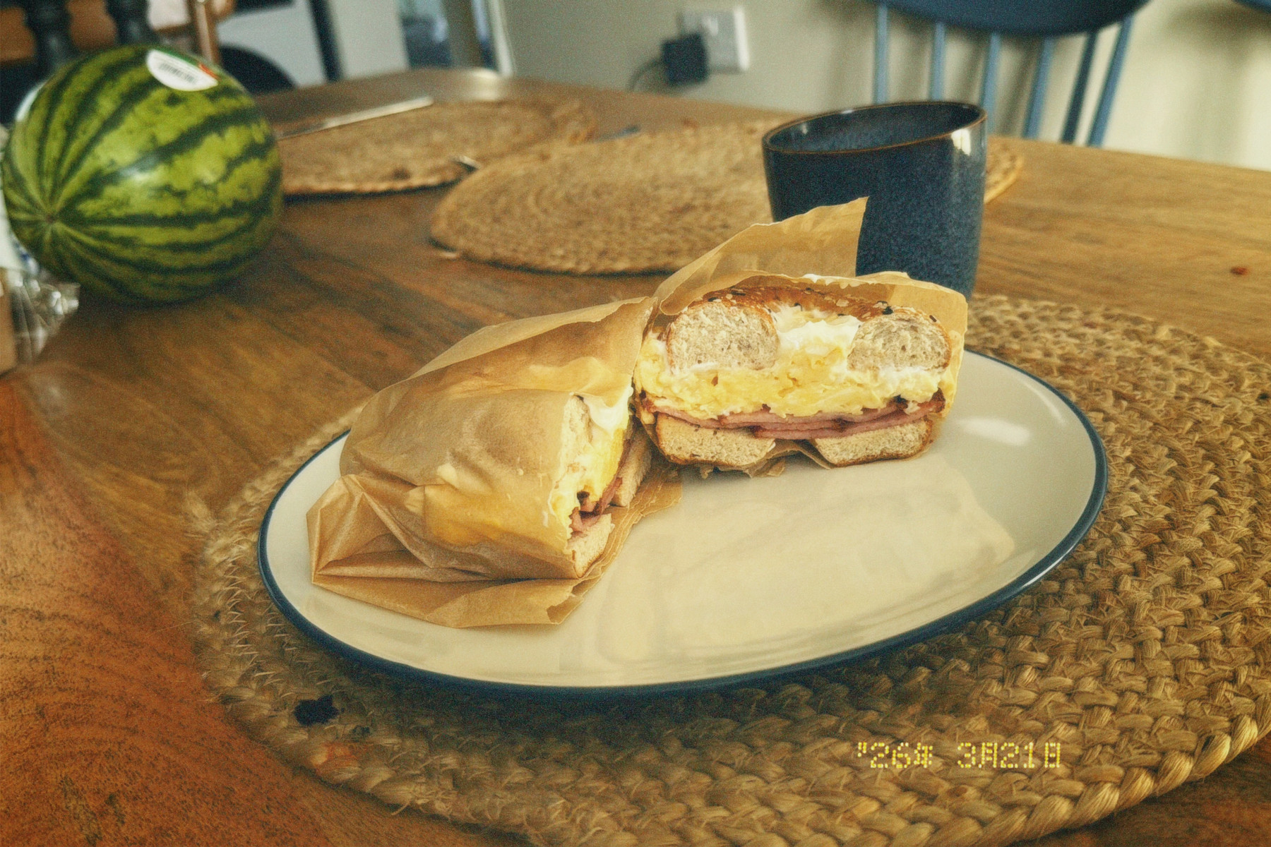 A breakfast bagel wrapped in paper on a plate with a cup of coffee.