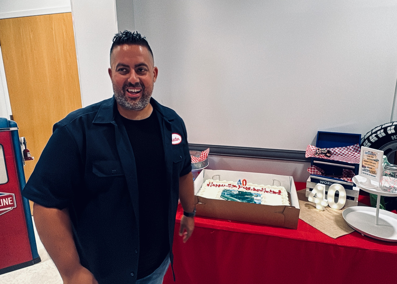 A man smiling to someone off camera in front of a birthday cake for his 40th birthday party