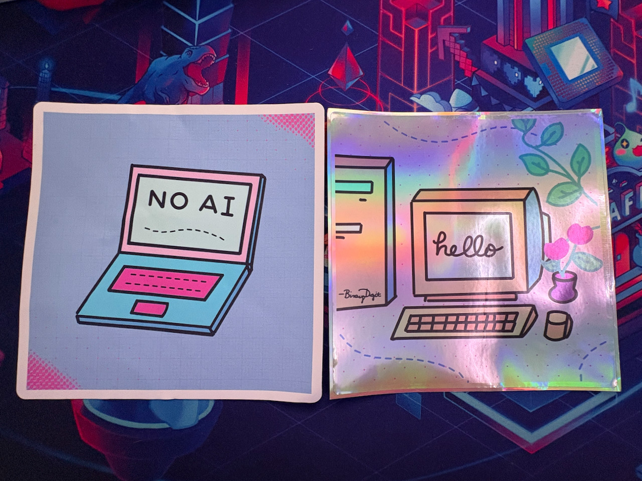 Two big sticker samples of my illustrations, including a “no ai” on a laptop and a “hello” computer on colorful backgrounds of blue, pink, teal and green.