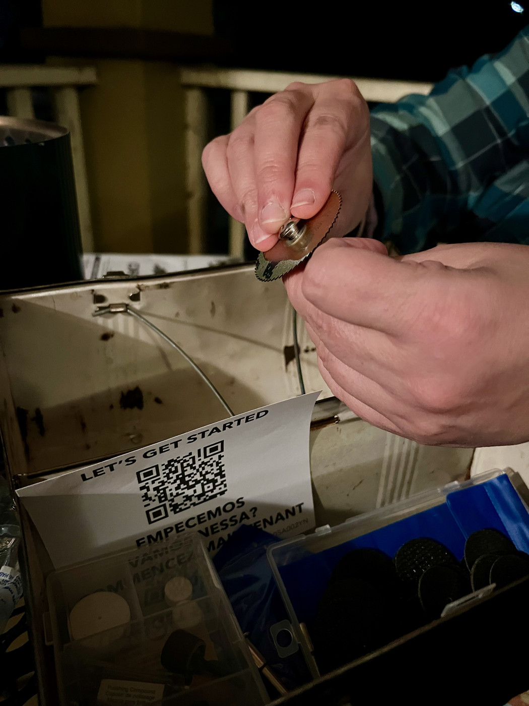 A pair of hands working a small circular blade onto the top of a Dremel.