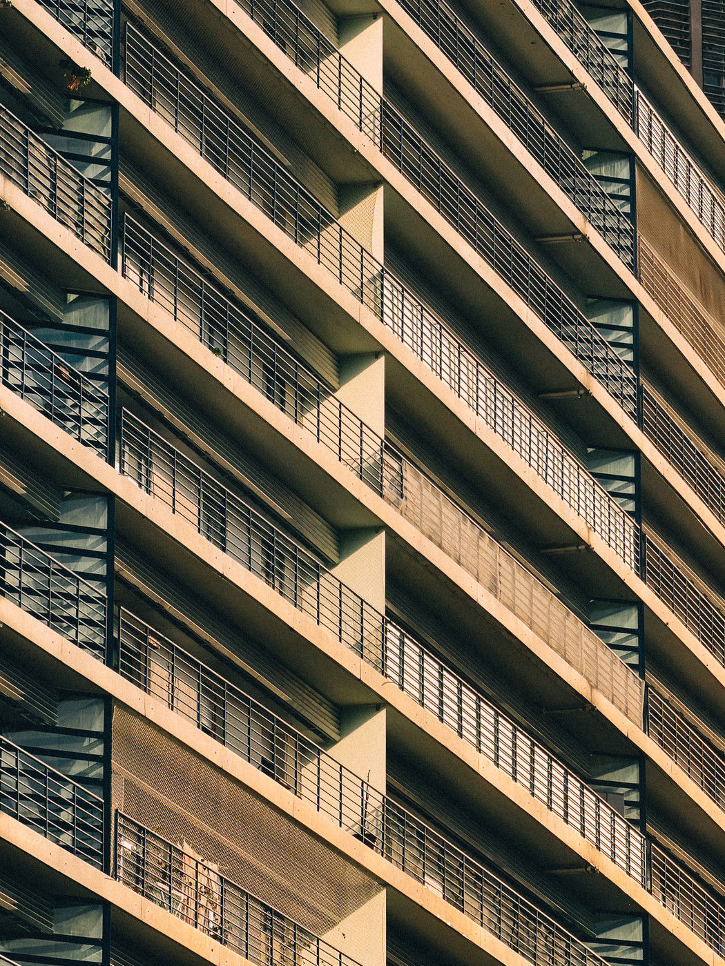 Close-up view of a modern high-rise building with repeating horizontal balconies and metal railings in warm sunlight.