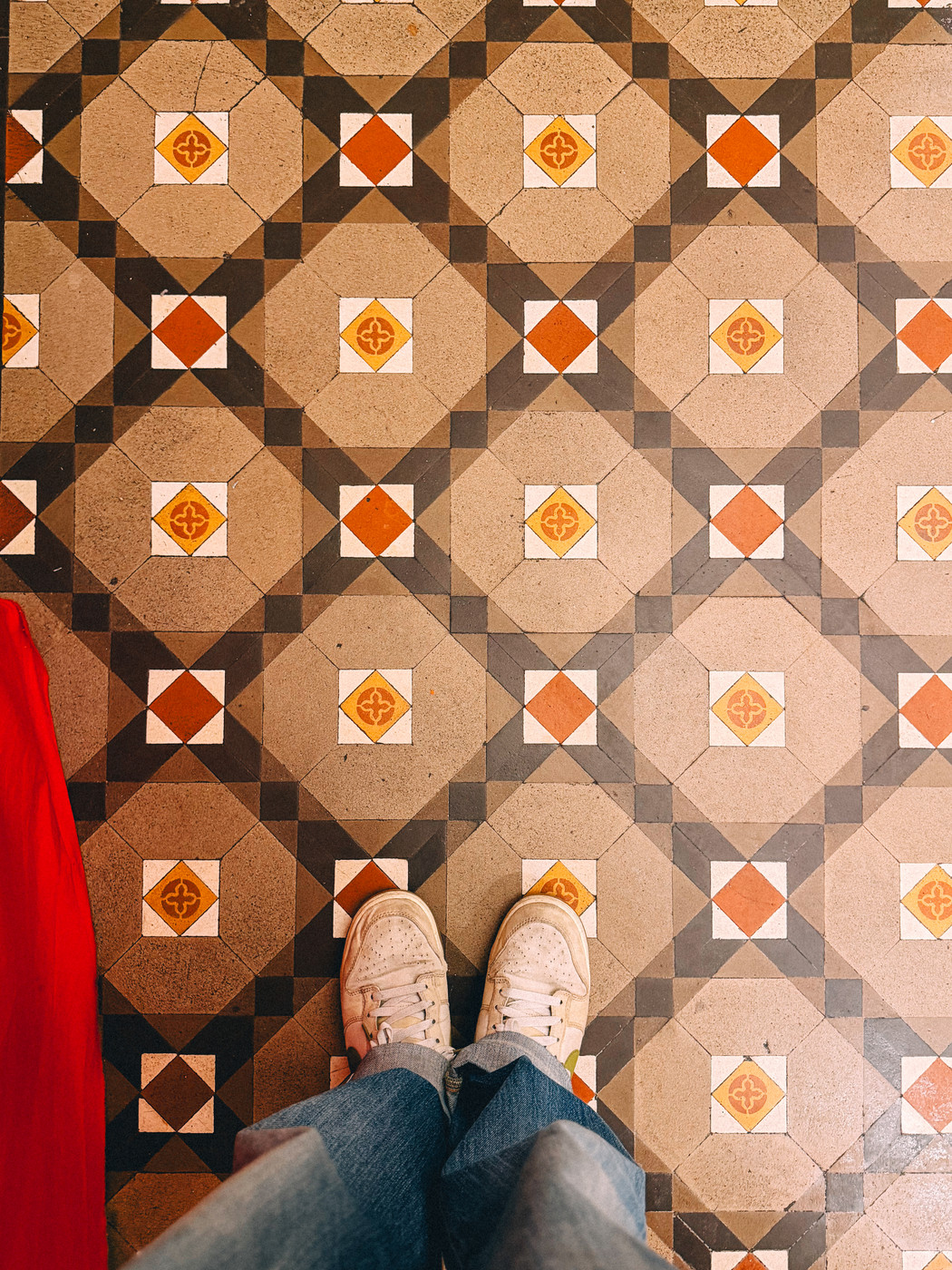 Person standing in white sneakers and jeans on a floor with colorful geometric patterns.