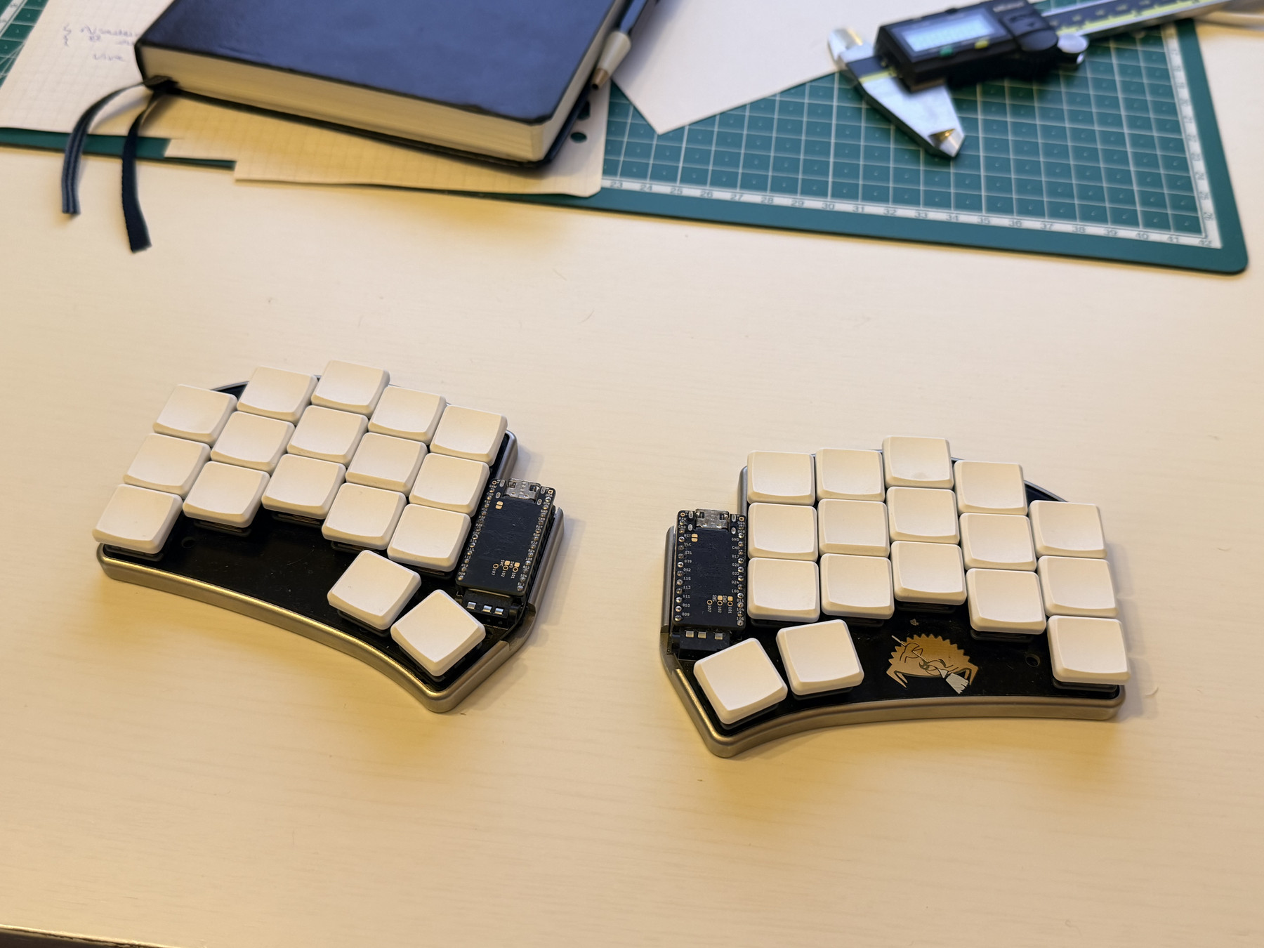 A split keyboard on a desk with various desk stuff in the background. The keyboard has two halves physically separate from each other. Each half has 17 keys for a total of 34 keys on the entire keyboard.