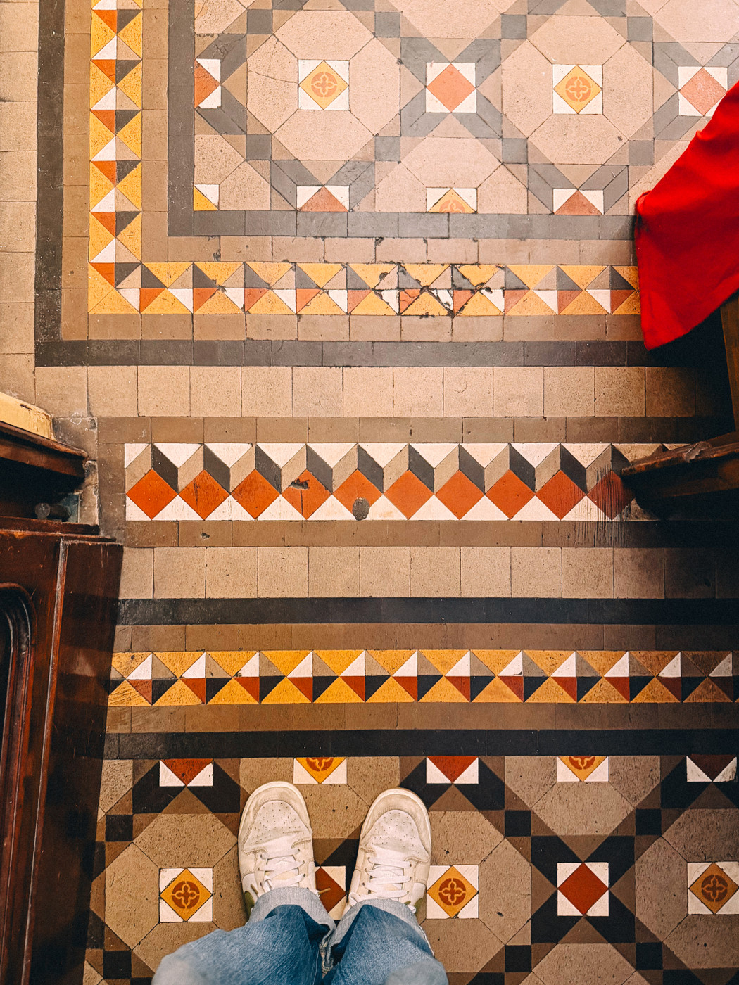 Person standing in white sneakers and jeans on a floor with colorful geometric patterns.