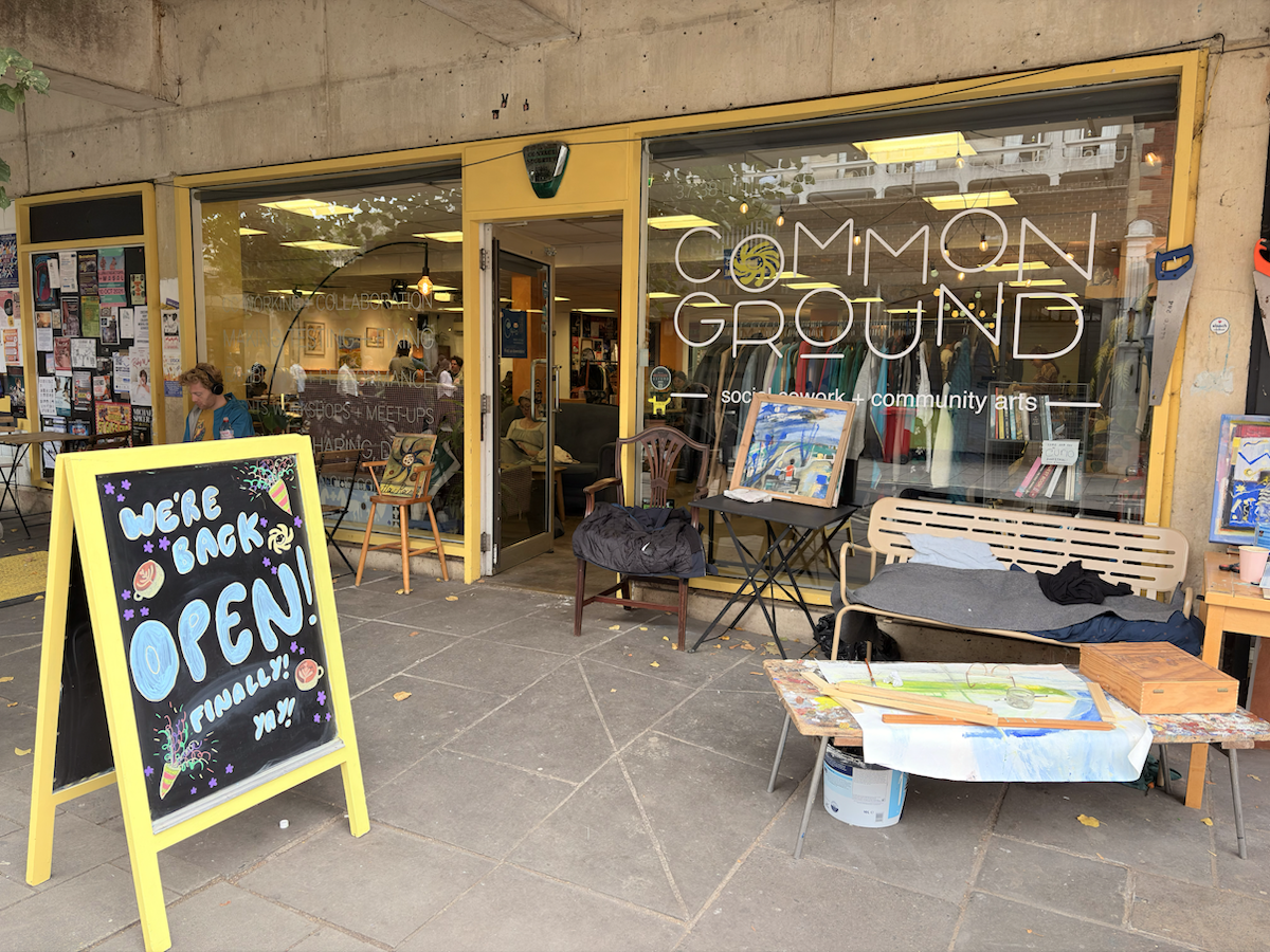 The front of a coffee shop with the words Common Ground written across the large window. An A-frame board outside says “We’re back Open!”
