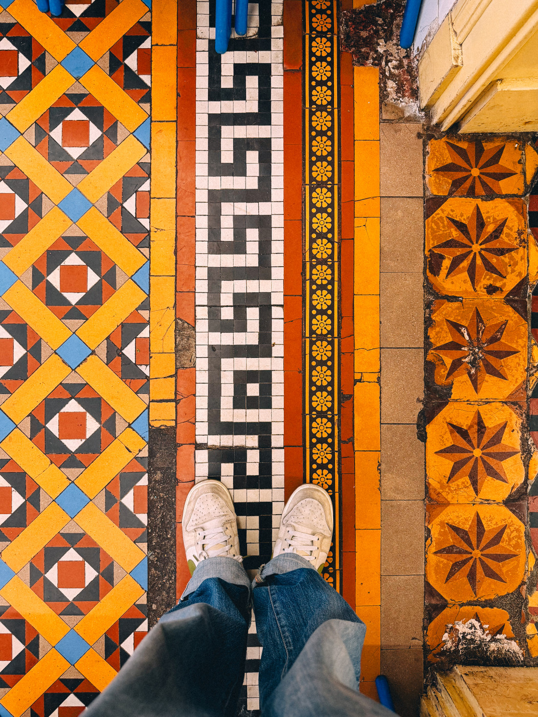 Person standing in white sneakers and jeans on a floor with colorful geometric patterns.
