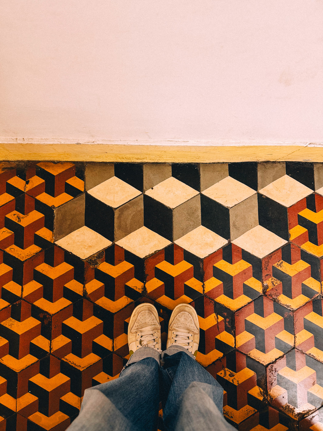 Person standing in white sneakers and jeans on a floor with colorful geometric patterns.