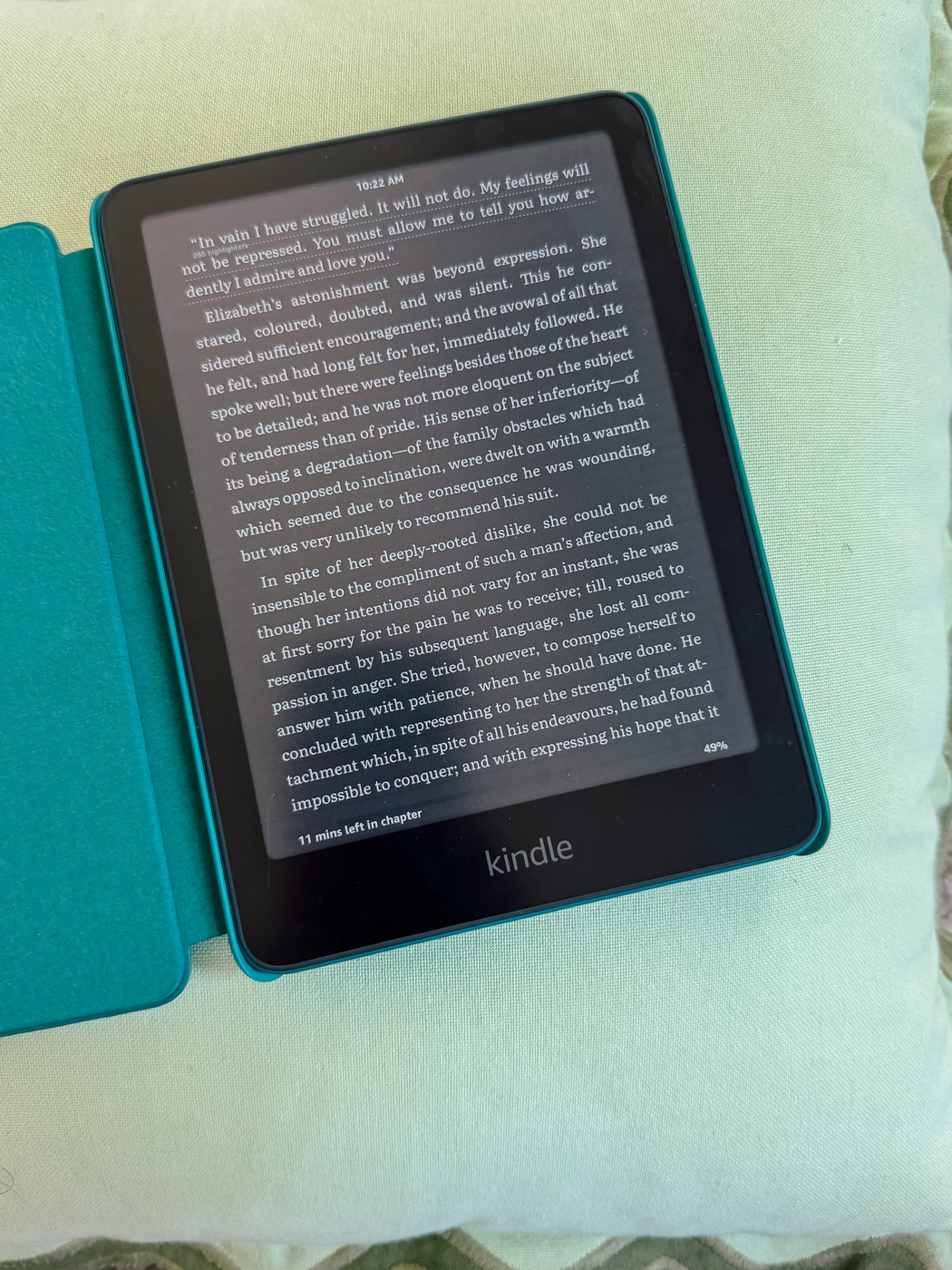 Auto-generated description: A Kindle with an open case is displaying text from a book, resting on a light green cushion.